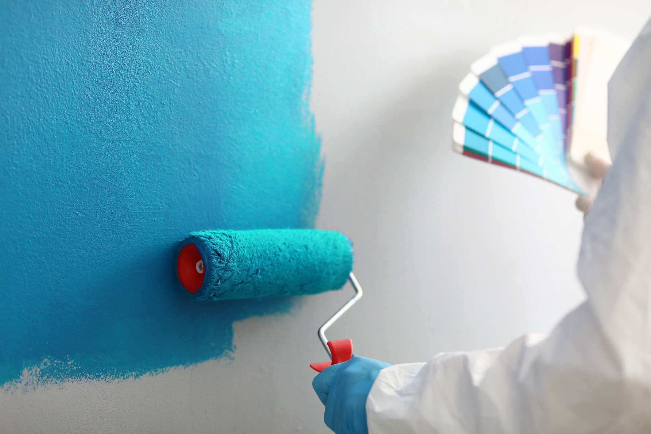 Turquoise Paint Application Interior Wall Turquoise paint being rolled onto white drywall with color swatch fan nearby during interior residential painting.