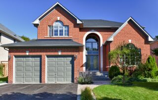 Red brick residential home with gray garage doors, blue arched entryway, and white trim accents