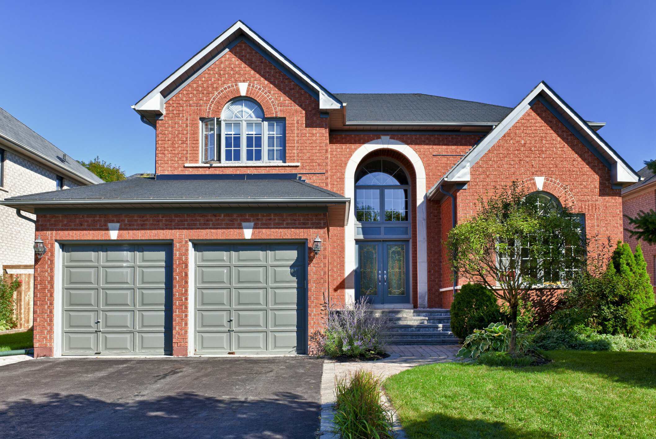 Brick Home Exterior Painting Red brick residential home with gray garage doors, blue arched entryway, and white trim accents