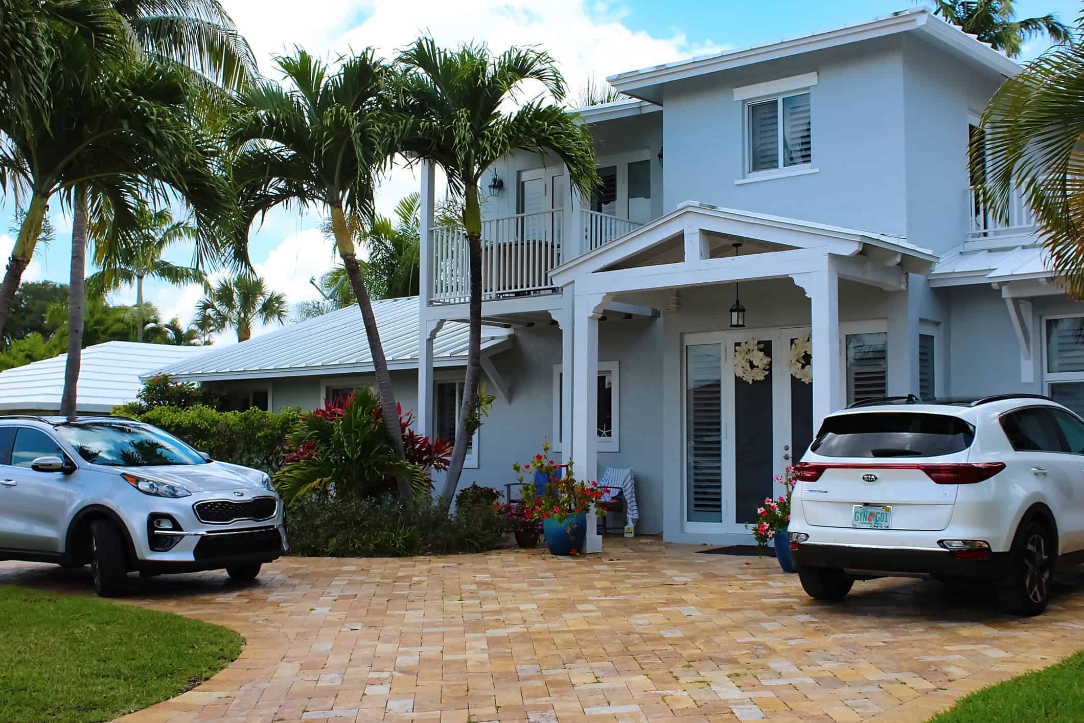 Light Blue Residential Home Exterior Light blue two-story residential home exterior with white trim, covered porch, and brick paver driveway.