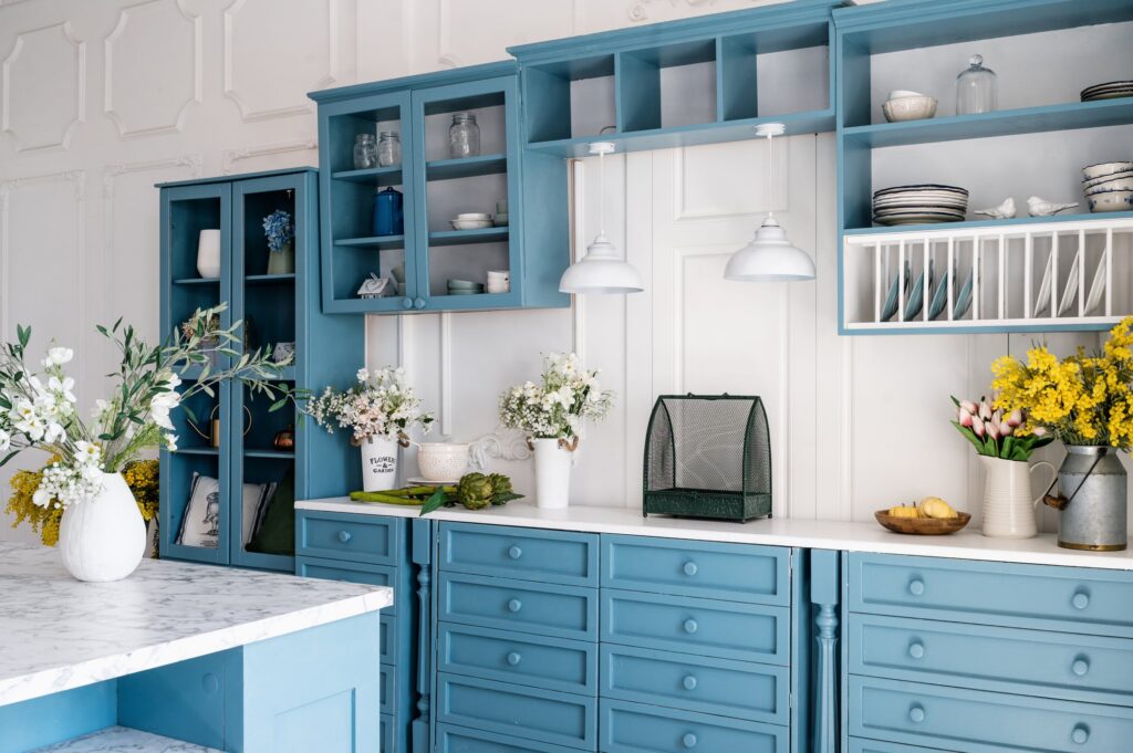 Teal Painted Kitchen Cabinetry Teal-painted kitchen cabinetry with white shiplap backsplash, marble countertop, open shelving, and white pendant lights
