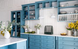 Teal-painted kitchen cabinetry with white shiplap backsplash, marble countertop, open shelving, and white pendant lights