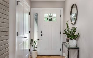 White-painted residential entryway with soft gray walls, white six-panel door, and hardwood flooring.