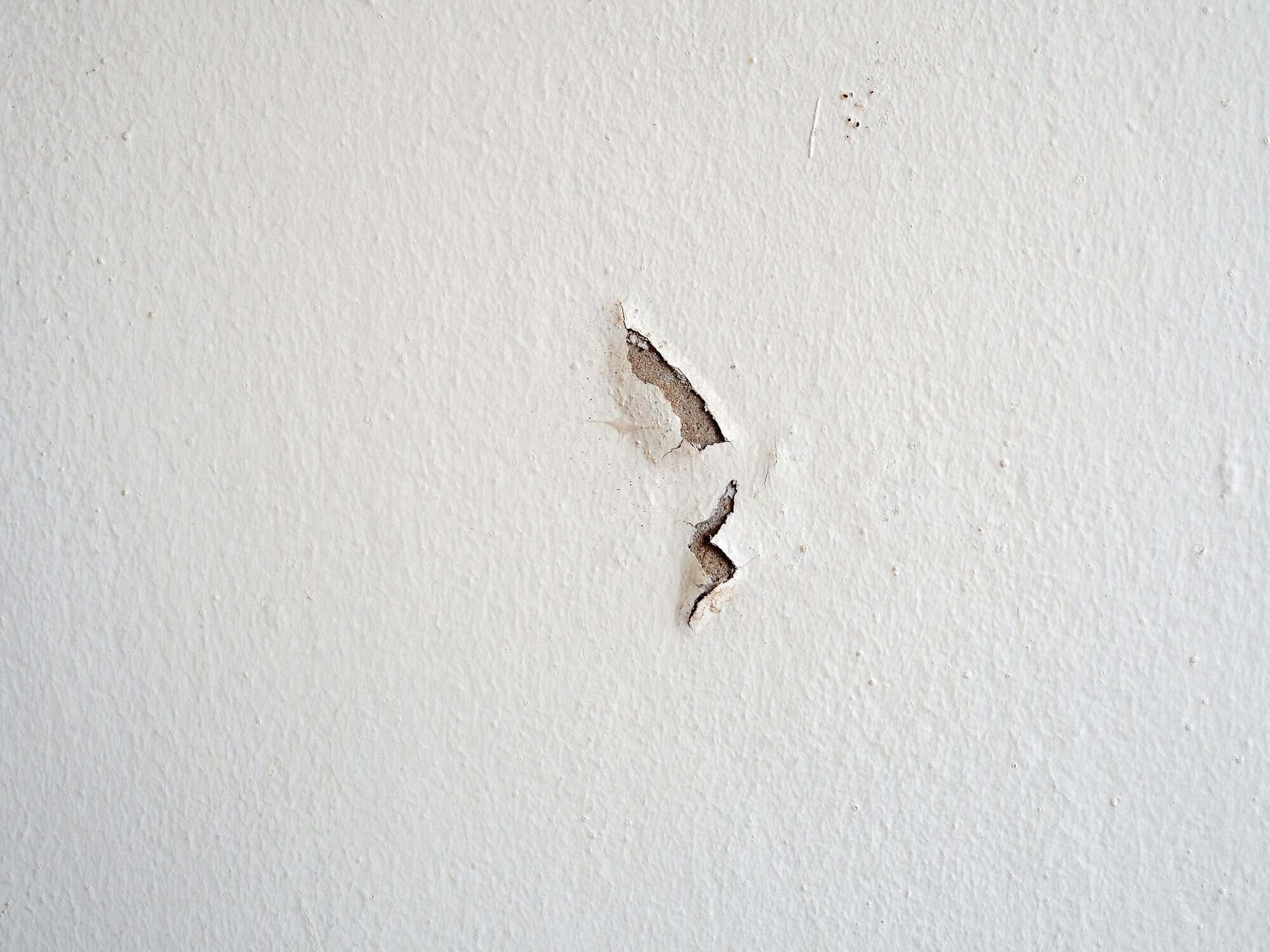 Drywall Crack Repair Preparation Jagged drywall crack with peeling paint and exposed joint compound on white interior wall surface.