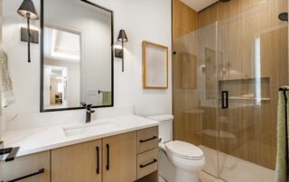 White quartz countertop with natural wood cabinetry, black-framed mirror, and glass shower enclosure in residential bathroom.