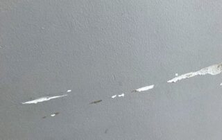 Gray drywall surface with multiple white paint cracks and brown damage streaks indicating joint compound separation.