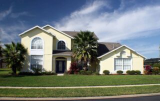 Cream-painted two-story residential home with white trim, arched windows, dark roof, and manicured front yard landscape