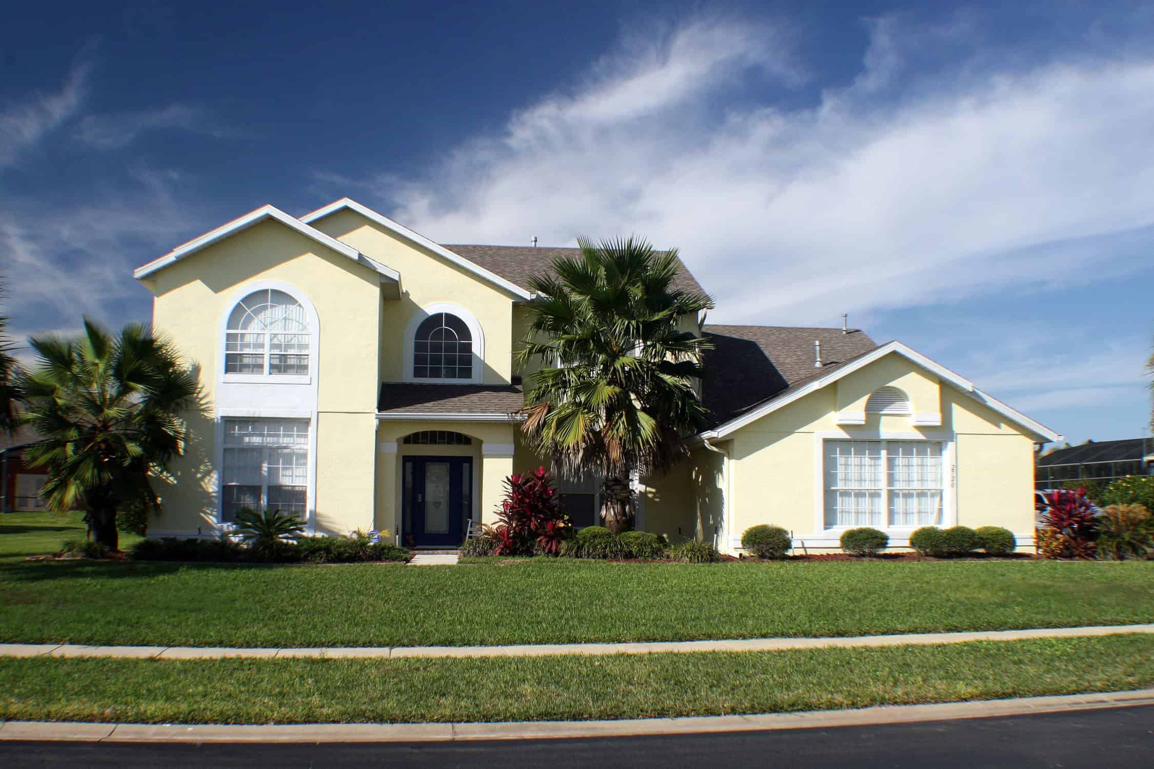 Cream Exterior Residential Home Cream-painted two-story residential home with white trim, arched windows, dark roof, and manicured front yard landscape