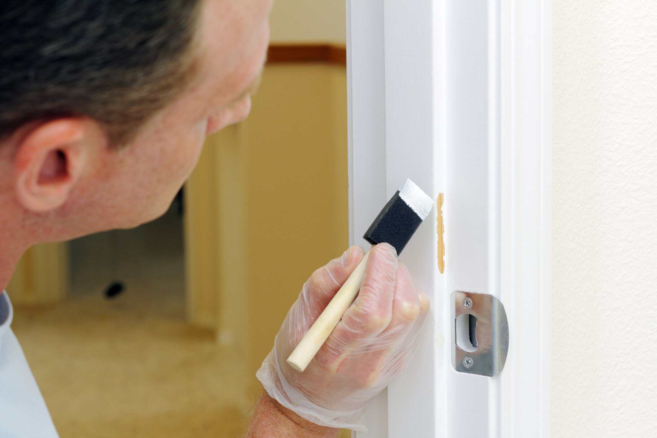 Interior Door Frame Painting Painter in clear plastic glove applying cream paint to white interior door trim with brush during residential painting.