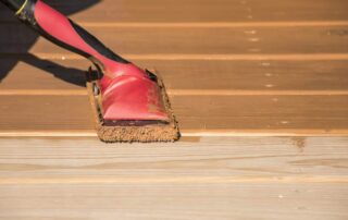 Red-stained paint brush with natural bristles applying color to light wood flooring during interior finishing.