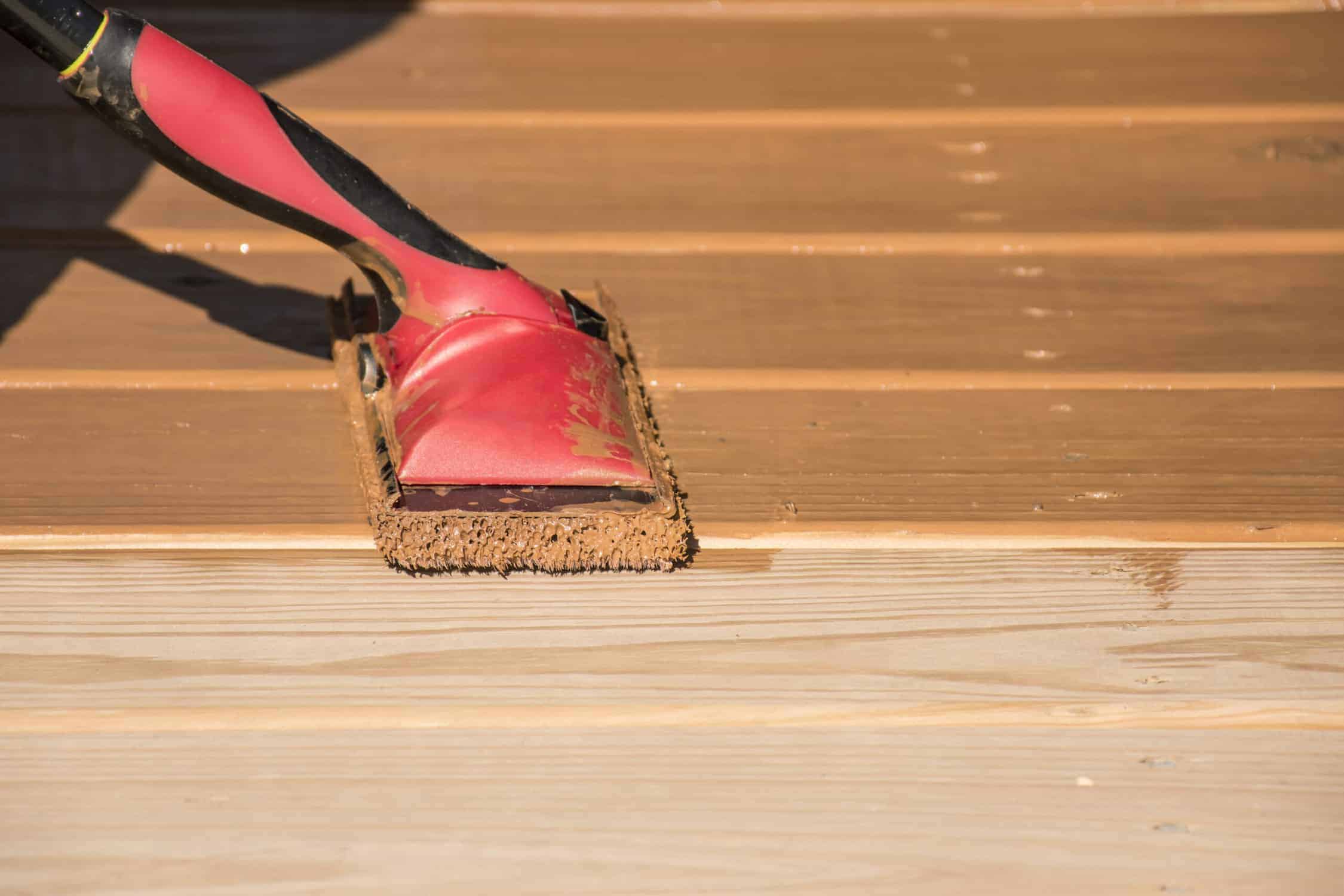 Red Wood Stain Brush Application Red-stained paint brush with natural bristles applying color to light wood flooring during interior finishing.