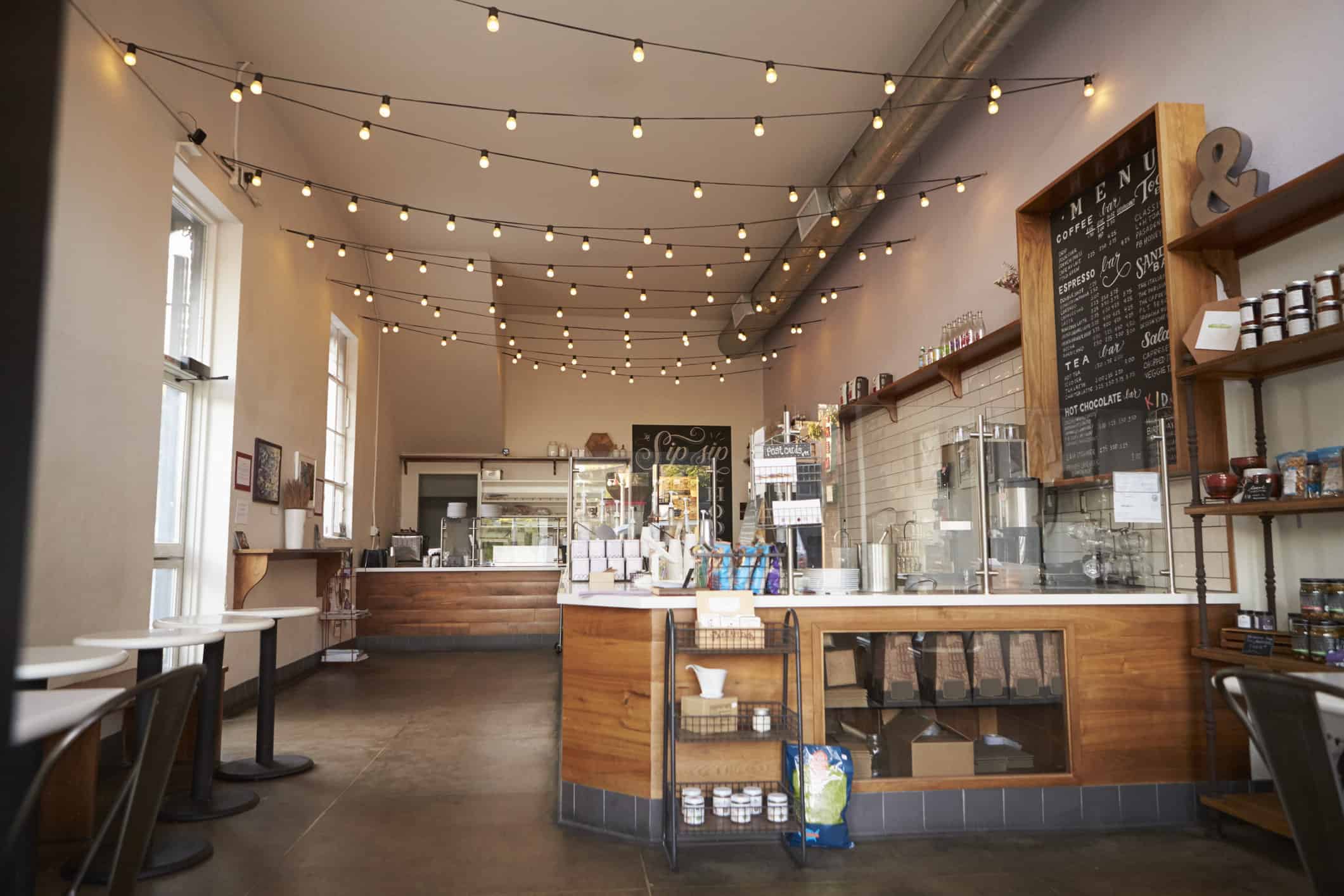 Tan Commercial Interior Cafe Tan-painted commercial interior cafe with warm string lighting, wood counter, black chalkboard menu, and large windows.