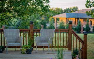 Red brick two-story residential home with dark roof, wood deck with railing, and mature trees in Saint Charles, IL