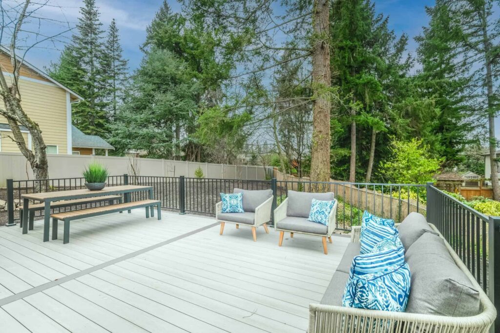 White Painted Residential Deck White-painted residential deck with black metal railings, gray upholstered seating, and forested backdrop.