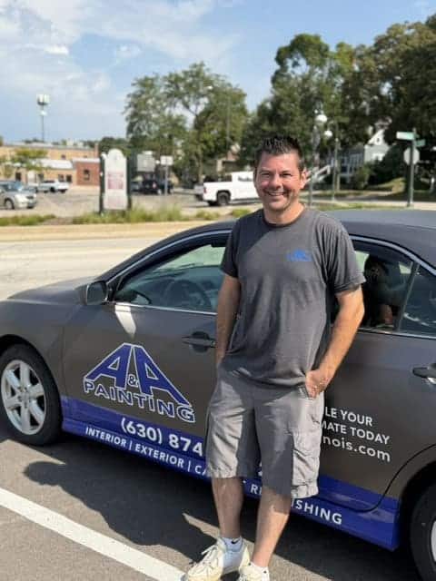 Man in gray t-shirt standing beside company work vehicle with blue logo and contact information in parking lot.