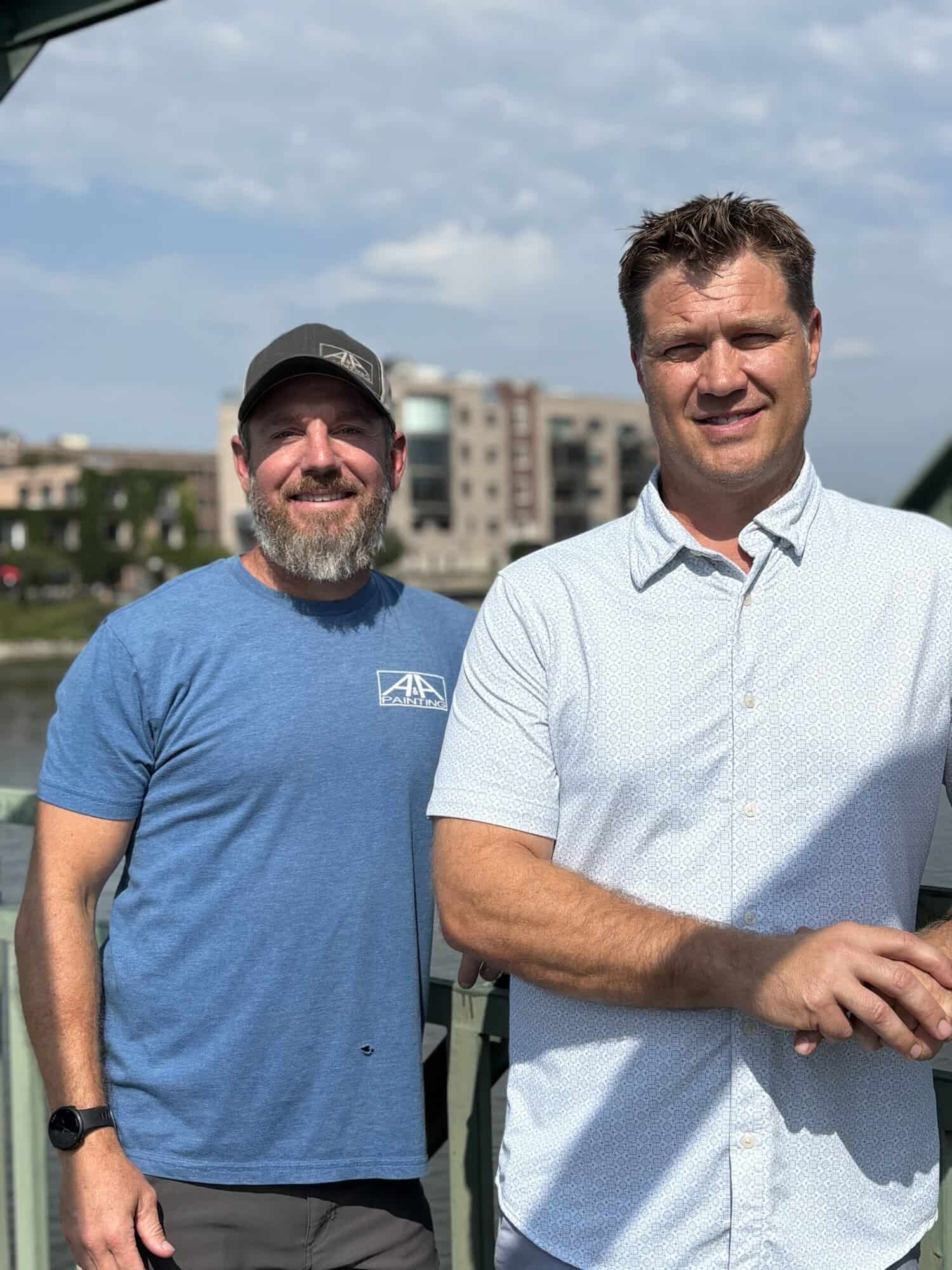 Painting Company Team Portrait Two men smiling on residential rooftop deck with waterfront and apartment buildings in background.