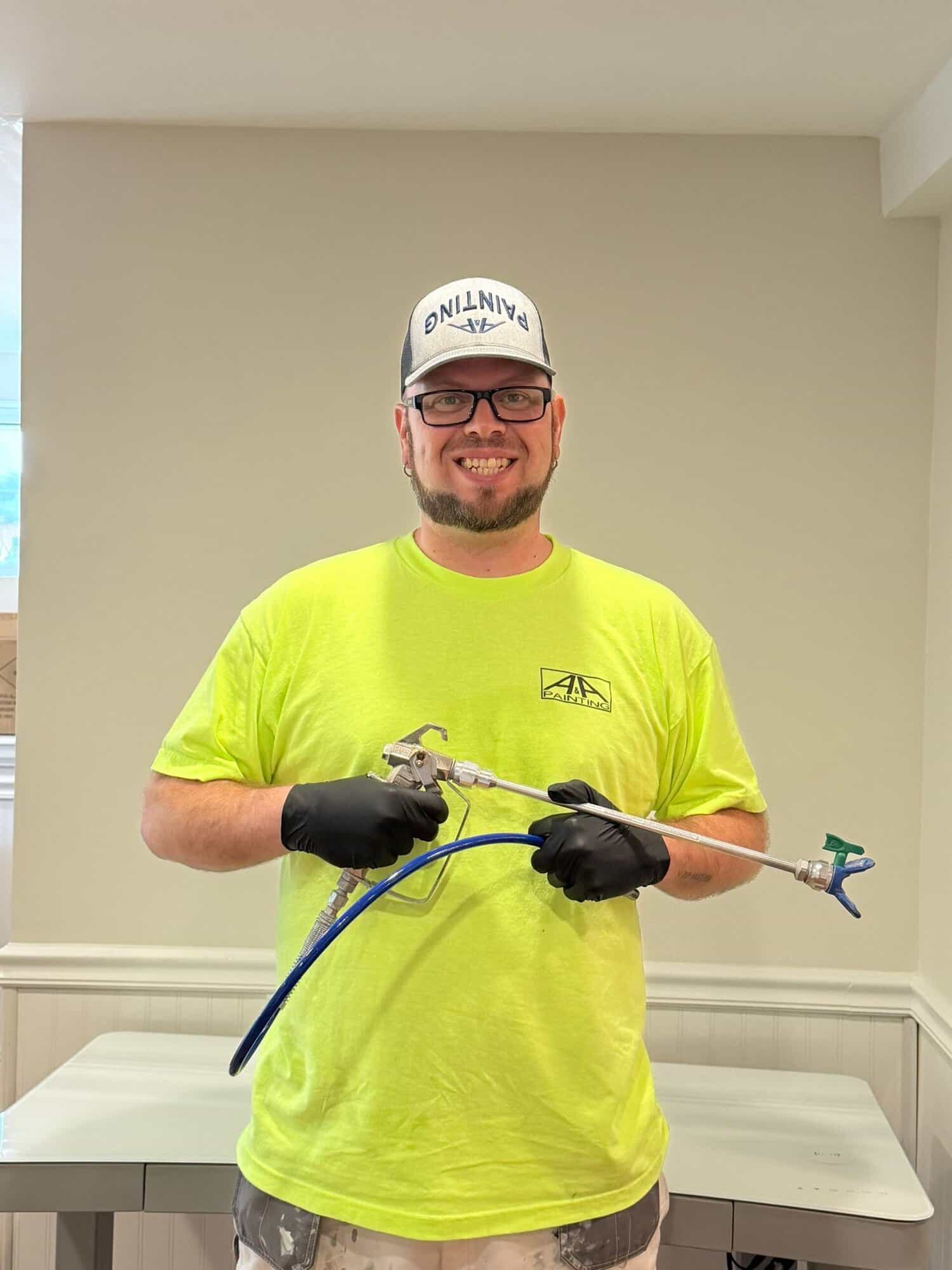 Painter in bright neon-yellow shirt and white baseball cap holding spray gun equipment with black gloves in cream interior