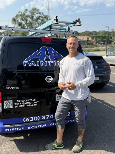 Man in white long-sleeve shirt standing in front of black work truck with company logo and contact information.
